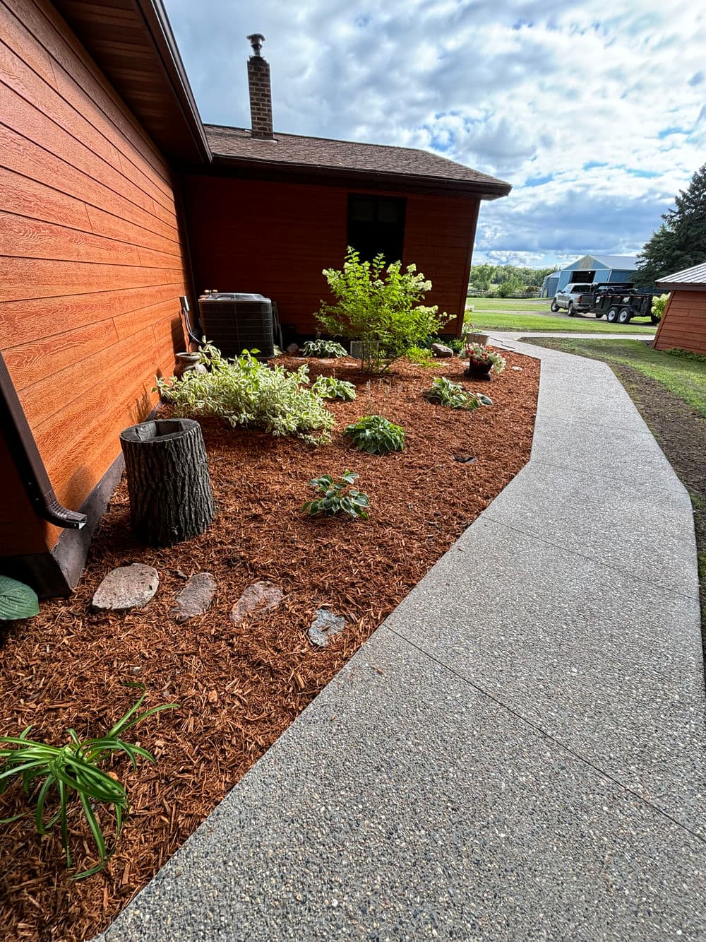 Lush garden with mulch, stepping stones, and vibrant plants beside a home pathway.