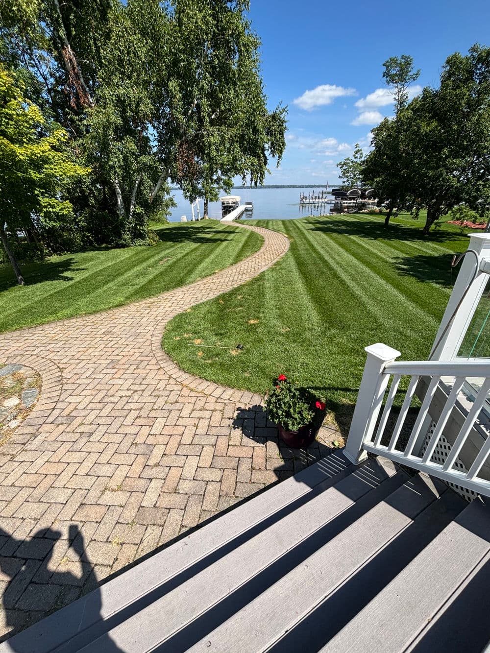 Scenic view of a pathway leading to a lake with lush green lawn and blue sky.
