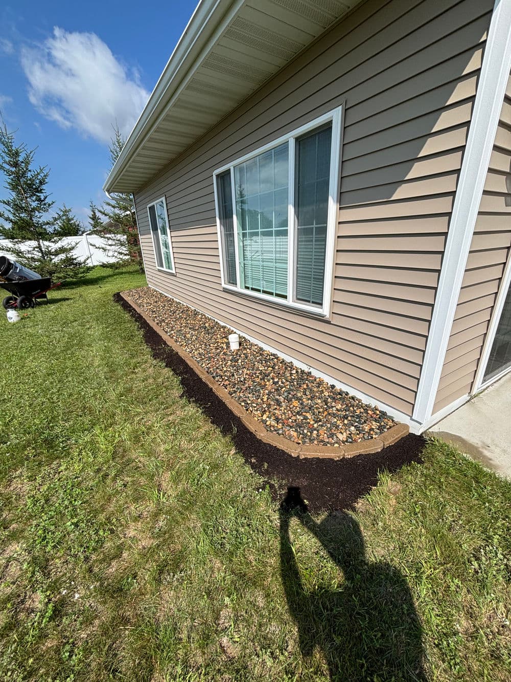Landscaped home exterior with gravel border, mulch, and lush green grass under a blue sky.